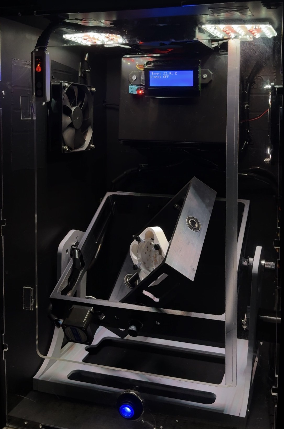 Random Positioning Machine inside an acrylic enclosure: a two-axis frame with a sample holder, full-spectrum LED lights, a fan and a display reading temperature
